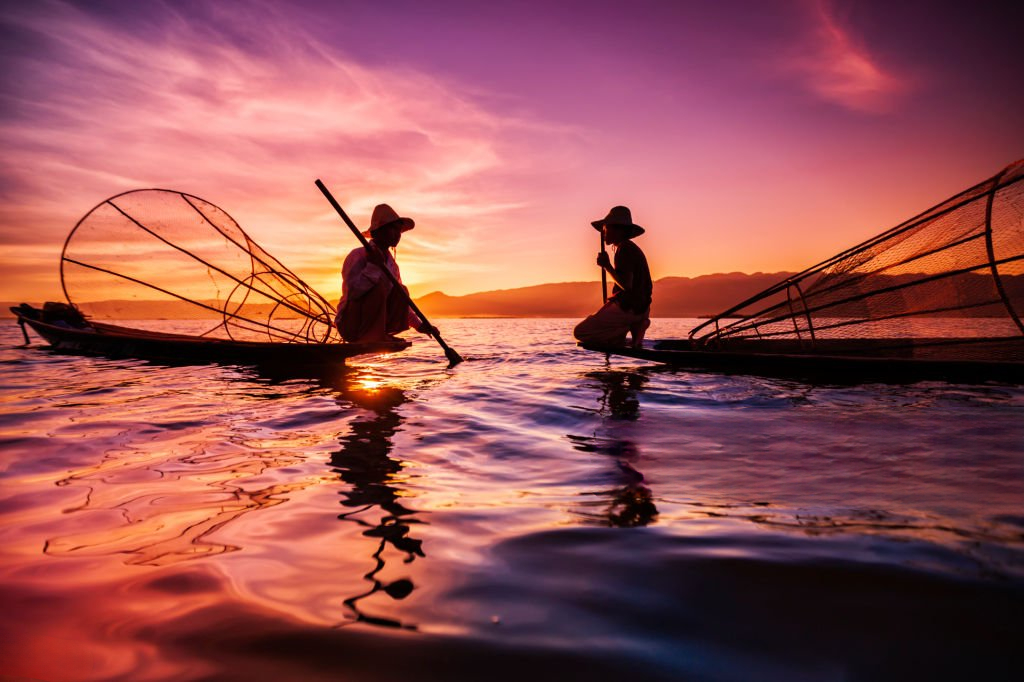 Scenic view of Inle Lake in Myanmar with traditional fishermen, floating gardens, and surrounding mountains under a clear sky