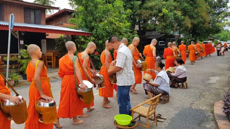Buddhist monks in saffron robes walking single file with alms bowls through a street in Myanmar